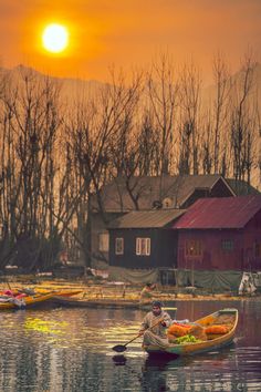 two people in a row boat on the water with houses and trees in the background