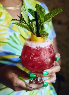 a woman holding a drink in her hand with a lime and mint garnish on it