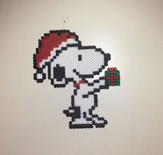 a cross stitch christmas ornament hanging on a wall with a dog wearing a santa hat and holding a candy cane