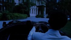 a man driving a car down a street next to a tall white building with lots of windows