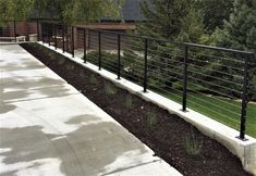 a black metal fence next to a sidewalk and grass area with trees in the background