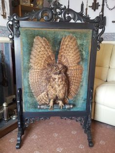 an owl sitting on top of a table in front of a framed picture with wings