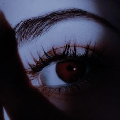 a woman's eye with long lashes and red eyeshade is reflected in the mirror