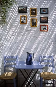 two chairs and a table in front of a wall with pictures on it