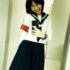 a woman in sailor's outfit looking at her cell phone while standing in a bathroom