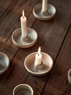 three lit candles sit in small dishes on a wooden table