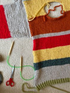 there is a knitted sweater and scissors on the floor next to yarn, needles and thread