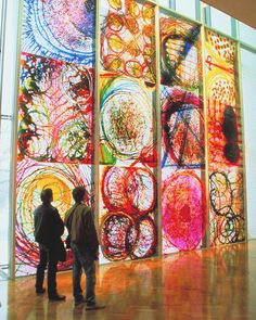 two people standing in front of an art piece that is brightly colored and has circles on it