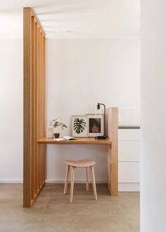 a small wooden desk in the corner of a room with white walls and flooring