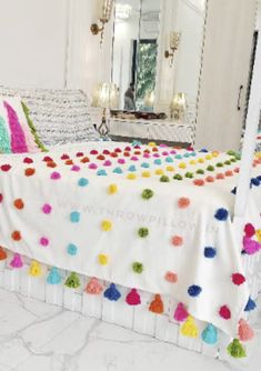 a white bed with colorful pom - poms on it and a mirror in the background