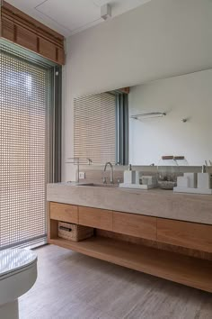 a bathroom with a sink, toilet and large window in the background that has wooden slats on it