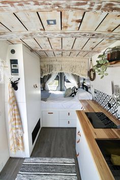 the interior of a camper with wood flooring and white walls, including a bed