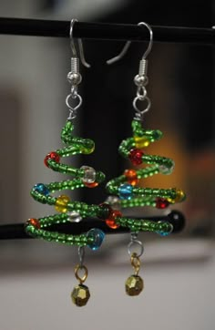 a pair of green and red beaded christmas tree earrings hanging from a black hook