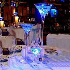 there are many glasses on the table with white linens and blue lights in the background