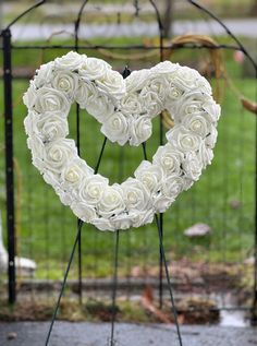 a heart - shaped wreath made out of white roses sits in front of a gate