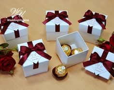 six white boxes with red ribbons and chocolates in them sitting on a wooden table