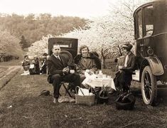 an old black and white photo of people sitting at a picnic table