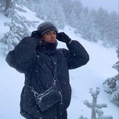 a man is standing in the snow talking on his cell phone while wearing a black jacket