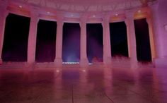 an empty room with columns and lights in the ceiling, lit up by purple lighting