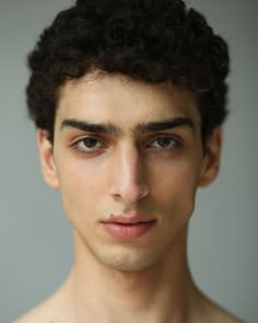 a young man with curly hair and no shirt is looking at the camera while posing for a portrait