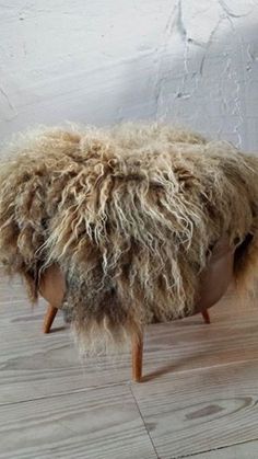 a sheep foot stool made out of wool on wooden floor next to white painted wall