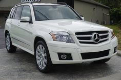 a white mercedes glk is parked in front of a dealership with the word motors written on it