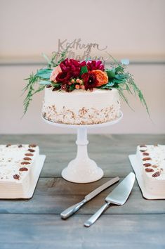 a white cake with flowers on top sitting next to two silver forks and knifes