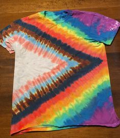 a tie - dyed t - shirt is laying on a wooden floor with the colors of rainbow and blue