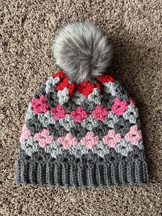 a crocheted hat with a pom - pom sits on the carpet