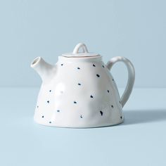 a white tea pot with blue speckles on it sitting on a light blue surface