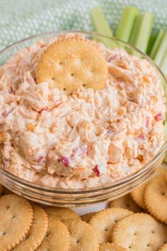 a bowl filled with crackers and dip surrounded by celery