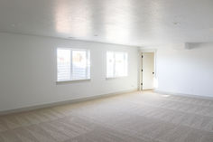 an empty room with two windows and carpet