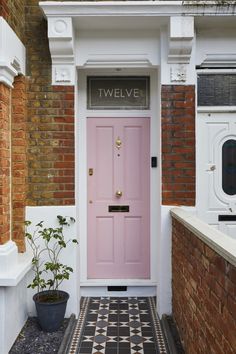 a pink door is in front of a brick wall and potted plant on the sidewalk