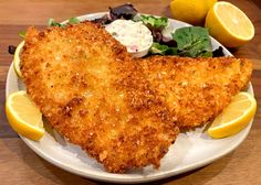 fried fish and salad on a plate with lemon wedges