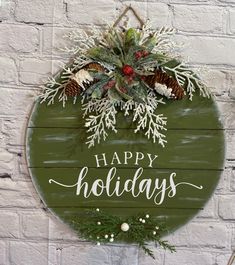 a sign that says happy holidays hanging on a brick wall with evergreens and pine cones