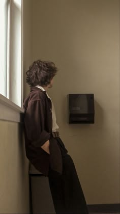 a woman leaning against a window sill looking out at the street and microwave on the wall