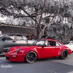 a red and white car parked in front of some cars on the side of the road