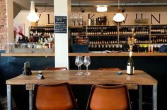 two brown leather chairs sitting at a wooden table in front of bottles and wine glasses