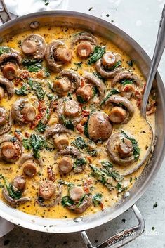 a pan filled with mushrooms and spinach on top of a white tablecloth next to silver utensils