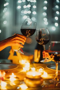 two people toasting wine glasses at a dinner table with lit candles in the background