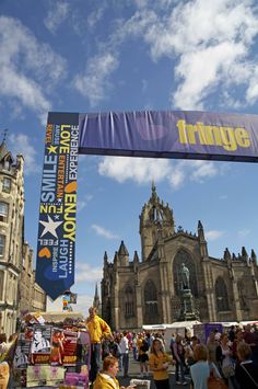 people are walking around in front of a large building with a banner hanging from it's side