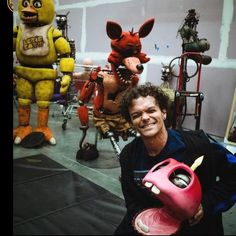 a man holding a pink toy in front of several stuffed animals and other stuff items