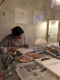 a woman sitting at a table with some papers and paintbrushes in front of her