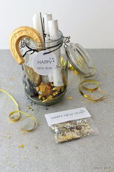 a jar filled with gold and silver confetti next to a tag that says happy new year