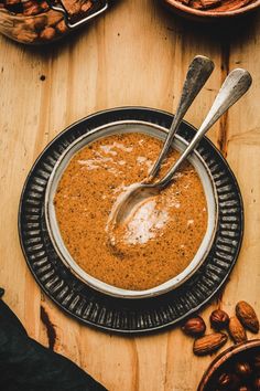 there is a bowl of soup on the table with nuts and spoons next to it