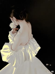 a woman in a white dress holding a flower and looking down at the ground with her back to the camera