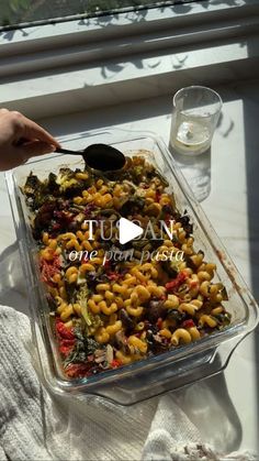 a person is holding a spoon over a casserole dish with pasta and spinach