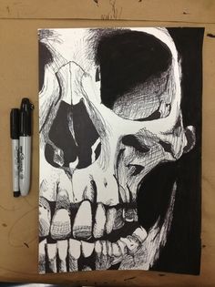 a black and white drawing of a skull on a piece of paper next to a pen