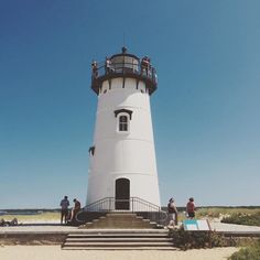 people are standing at the top of a white light house with stairs leading up to it