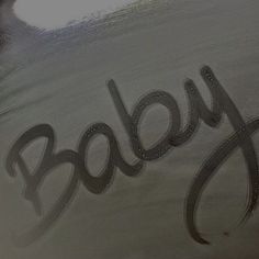 the word baby written in cursive black ink on a shiny metal surface,